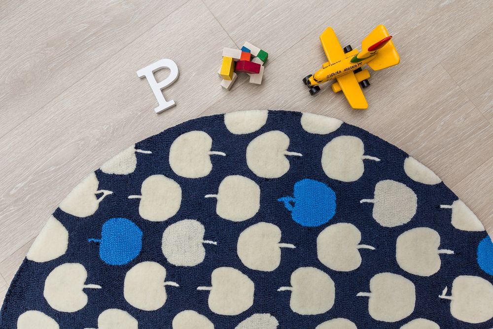 Dark navy round rug with apple pattern beside letter P and colorful toy airplane.
