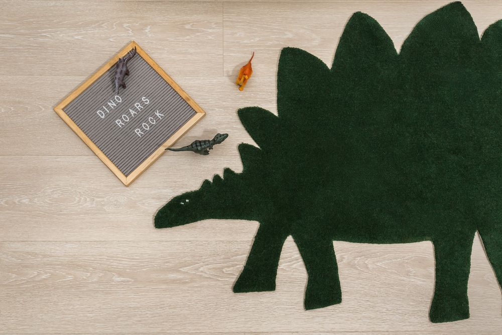 Dark green stegosaurus shaped dinosaur rug on light wood floor next to a letter board saying Dino Roars Rock.