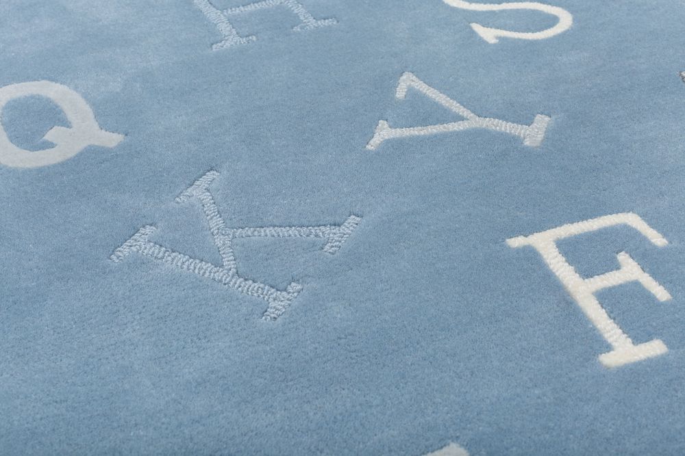 Close-up of blue alphabet rug showing embossed letters Q, Y, W, V, E in white and grey tones.