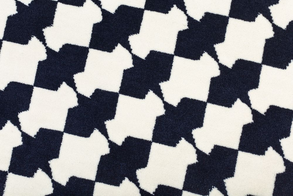 Close-up of navy blue and white geometric houndstooth cross pattern on a soft textured rug.