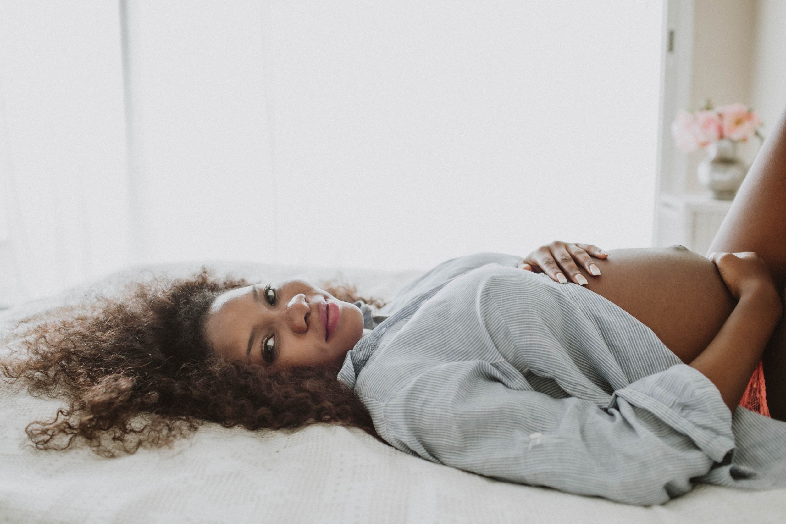 Backlit maternity photo of a dark-skinned mother lying down, capturing serene, intimate, and elegant pregnancy moments.