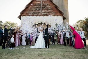 Wedding party celebrates with confetti outside a rustic barn chapel.