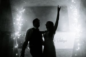Silhouettes of people dancing against bright sparklers and lights at a nighttime event.