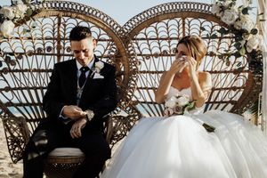 Wedding ceremony setup with ornate metal arch and floral decorations against blue sky.