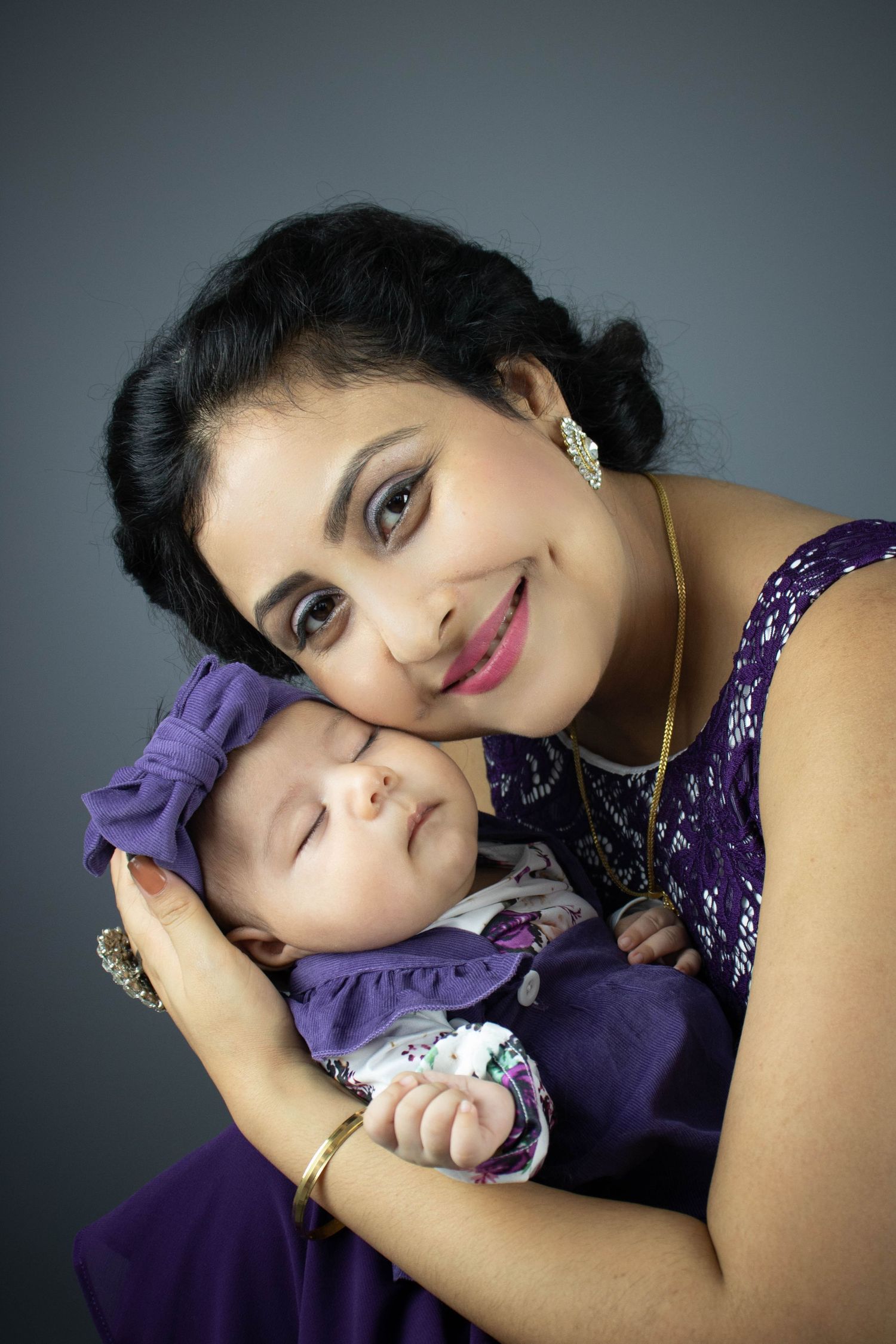 mother lovingly holding baby daughter in matching coordinated purple outfits for mother and baby photo shoot
