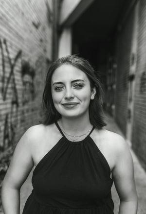 Black and white portrait of woman in dark halter top against urban brick wall.