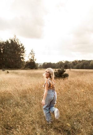 Portrait in a golden wheat field at sunset wearing overalls and looking to the side.