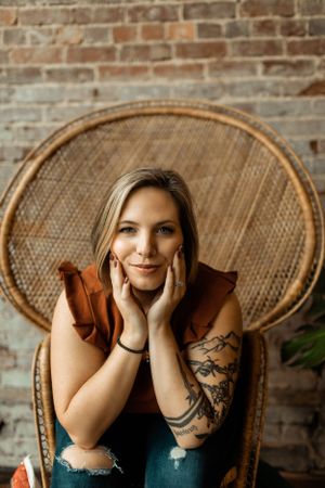 Person in rattan chair showing artistic tattoos against industrial brick backdrop.