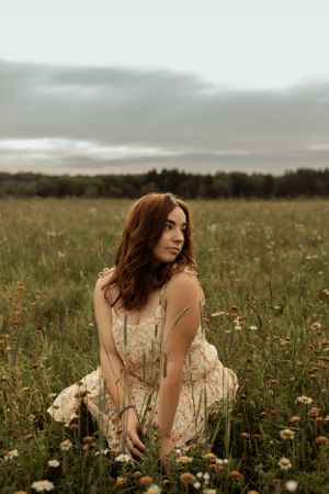 Figure in vintage dress kneeling among wildflowers in misty field.