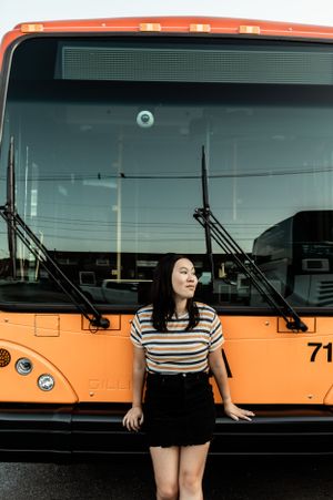 Musician in striped shirt poses in front of orange public transit bus.