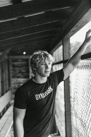 Black and white portrait of athletic model in Gymshark shirt leaning against fence.