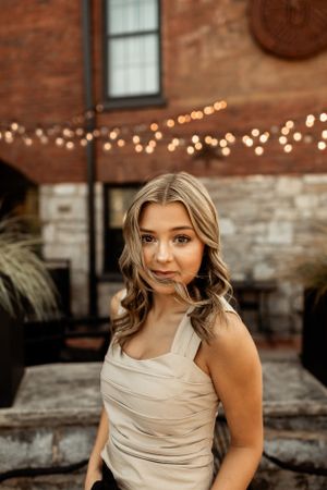 Portrait against brick wall with string lights and warm evening ambiance.