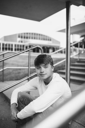 Black and white portrait of student sitting on modern campus steps.