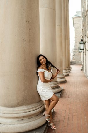Woman in white dress posing against classical stone columns.