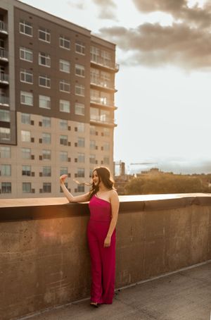Woman in red jumpsuit poses on rooftop during golden hour sunset.