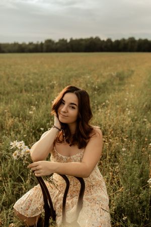 Portrait in floral dress sitting in wildflower meadow at golden hour.
