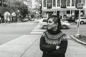 Urban street portrait with a patterned sweater against city architecture.