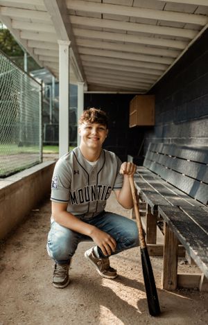 Baseball player with bat crouches in wooden dugout wearing Mounties uniform.