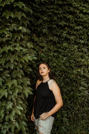 Woman in black halter top poses against wall of lush green ivy.