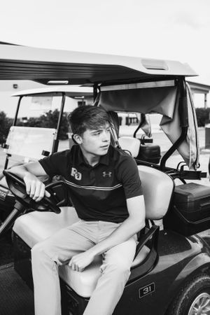 Athlete in casual attire sitting on golf cart in black and white.