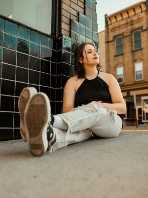Woman in black top sitting against tiled wall in urban setting.