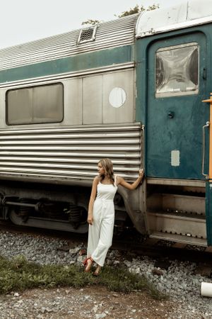 Person in white outfit posing against vintage train car exterior.