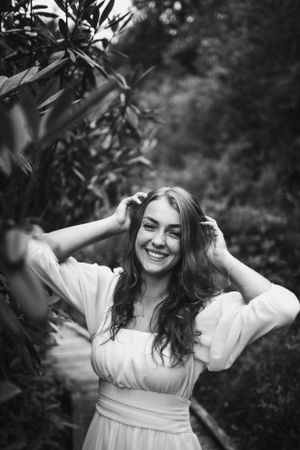 Black and white portrait of a woman in a white dress smiling joyfully in a garden setting.