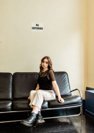 Casual portrait on black leather couch beneath No Loitering sign.