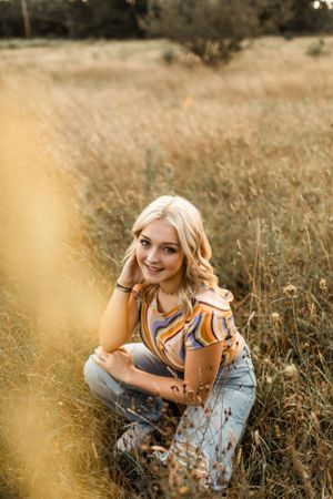 Portrait of woman in floral top sitting in golden sunlit field of tall grass.