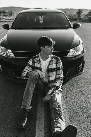 Casual automotive portrait with person sitting on hood of black sedan.