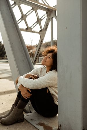 Artistic portrait against industrial metal structure wearing white sweater and boots.