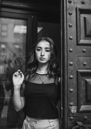 Dramatic black and white portrait against a heavy wooden door with metal rivets.