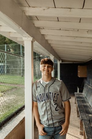 Baseball player wearing Mounties jersey number 2 poses in dugout.