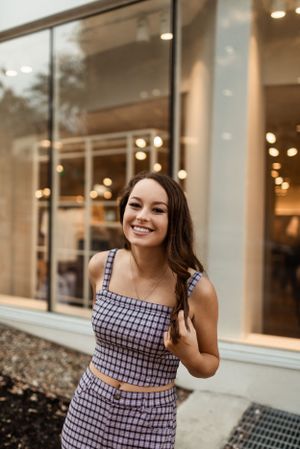 Candid outdoor portrait in checkered outfit with storefront windows.