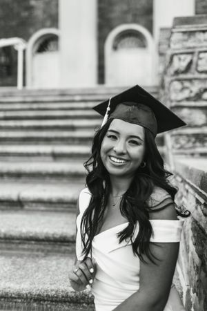 Black and white graduation portrait on steps with cap and gown.