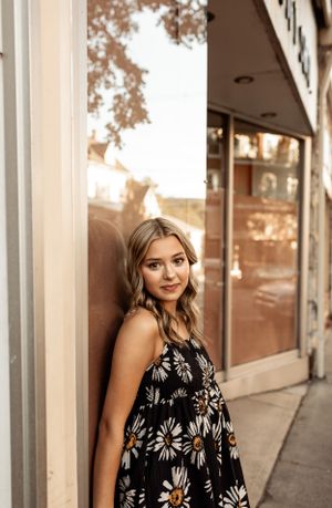 Outdoor portrait in floral dress against storefront at sunset.