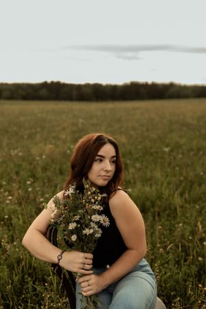 Portrait in a wildflower meadow at sunset holding a bouquet of fresh wildflowers.