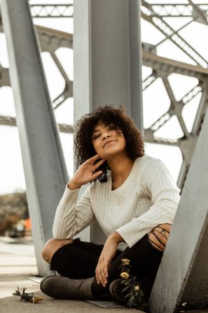 Casual portrait against metal bridge structure in natural lighting.