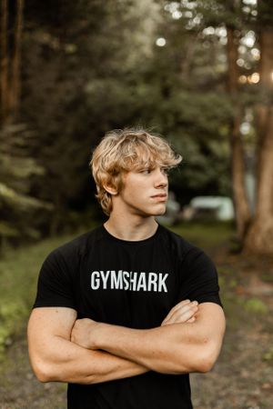 Athletic model in black Gymshark t-shirt poses outdoors with crossed arms.