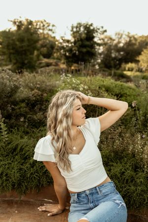 Outdoor portrait pose against greenery in white top and blue jeans.