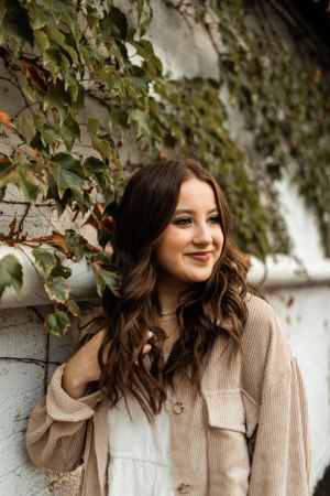 Portrait against ivy-covered wall features casual sweater and natural wavy hair styling.