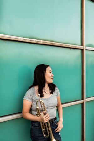 Musician with trumpet poses against turquoise wall with geometric lines.