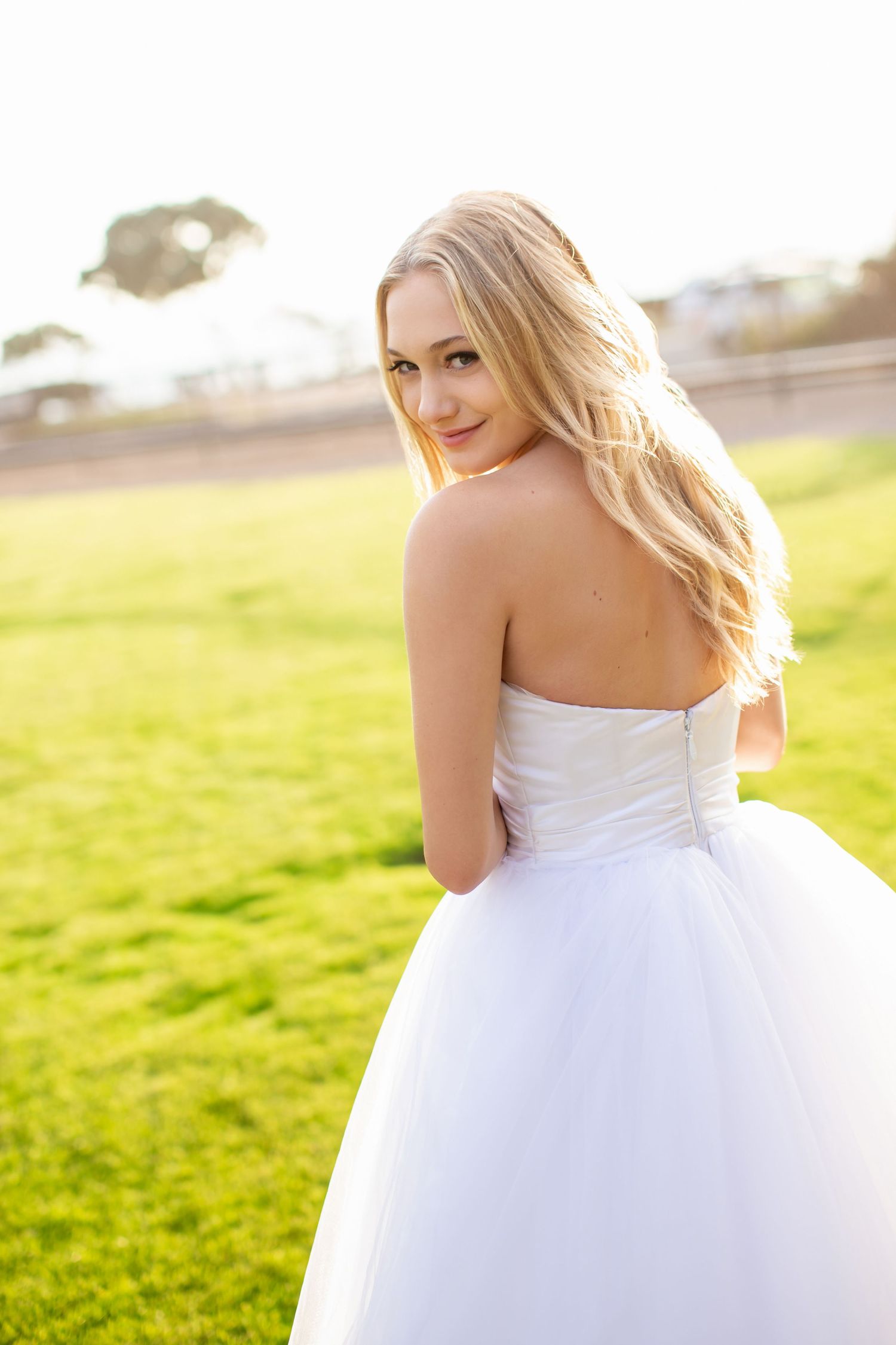 Bridal portrait in flowing white gown during golden hour in grassy field.