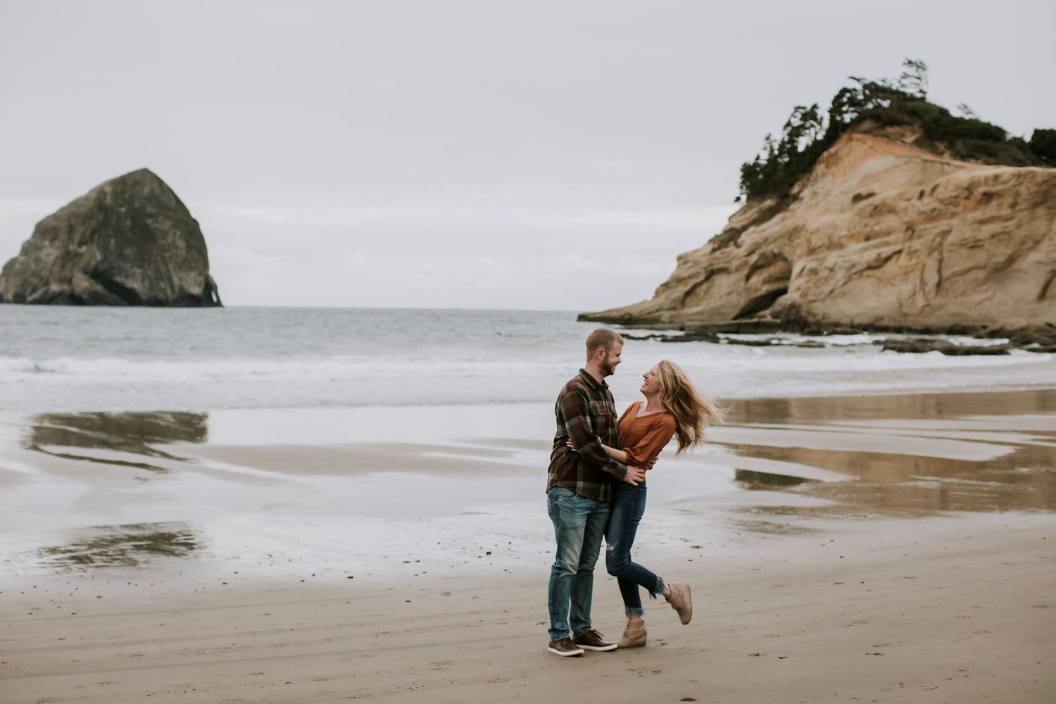 Boy in plaid and girl in orange looking at each other on the sand at the beach