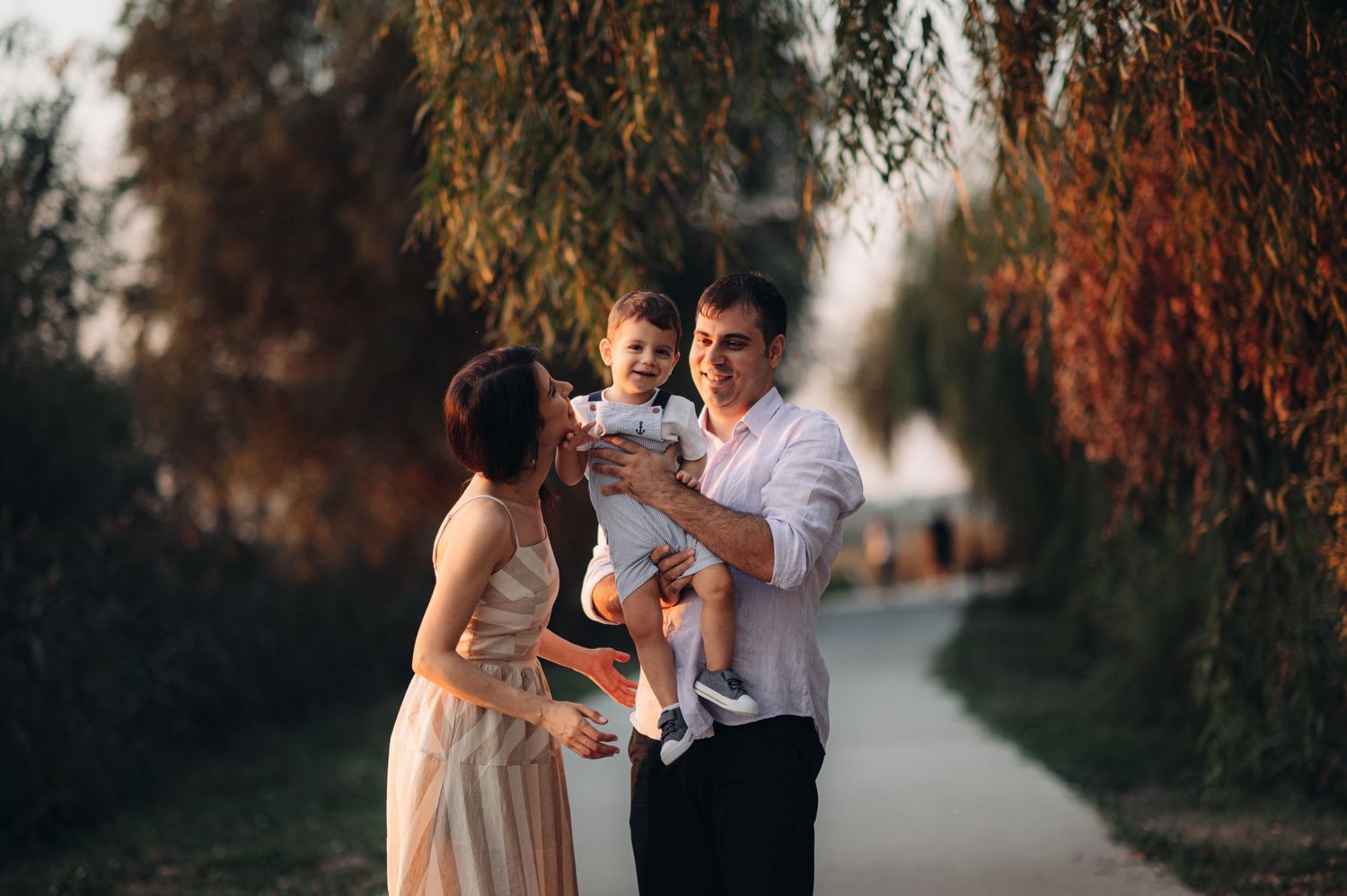 A family having a playful moment together on a tree-lined pathway at dusk.