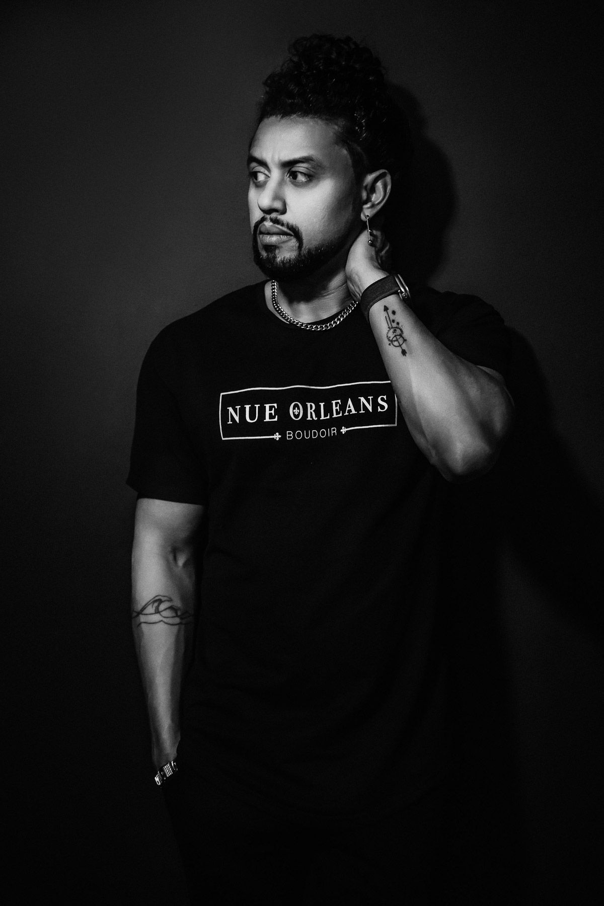 Black and white portrait of person wearing Nue Orleans t-shirt against dark background.