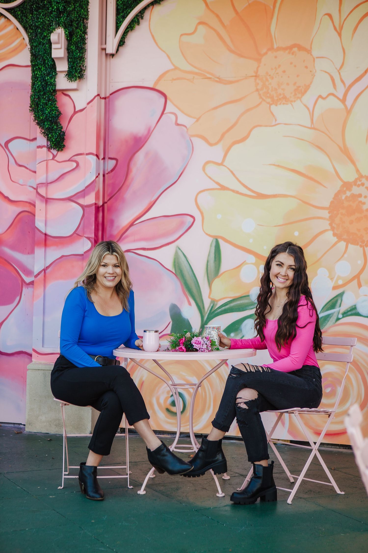 Two women enjoying coffee at a cafe with vibrant floral mural backdrop.