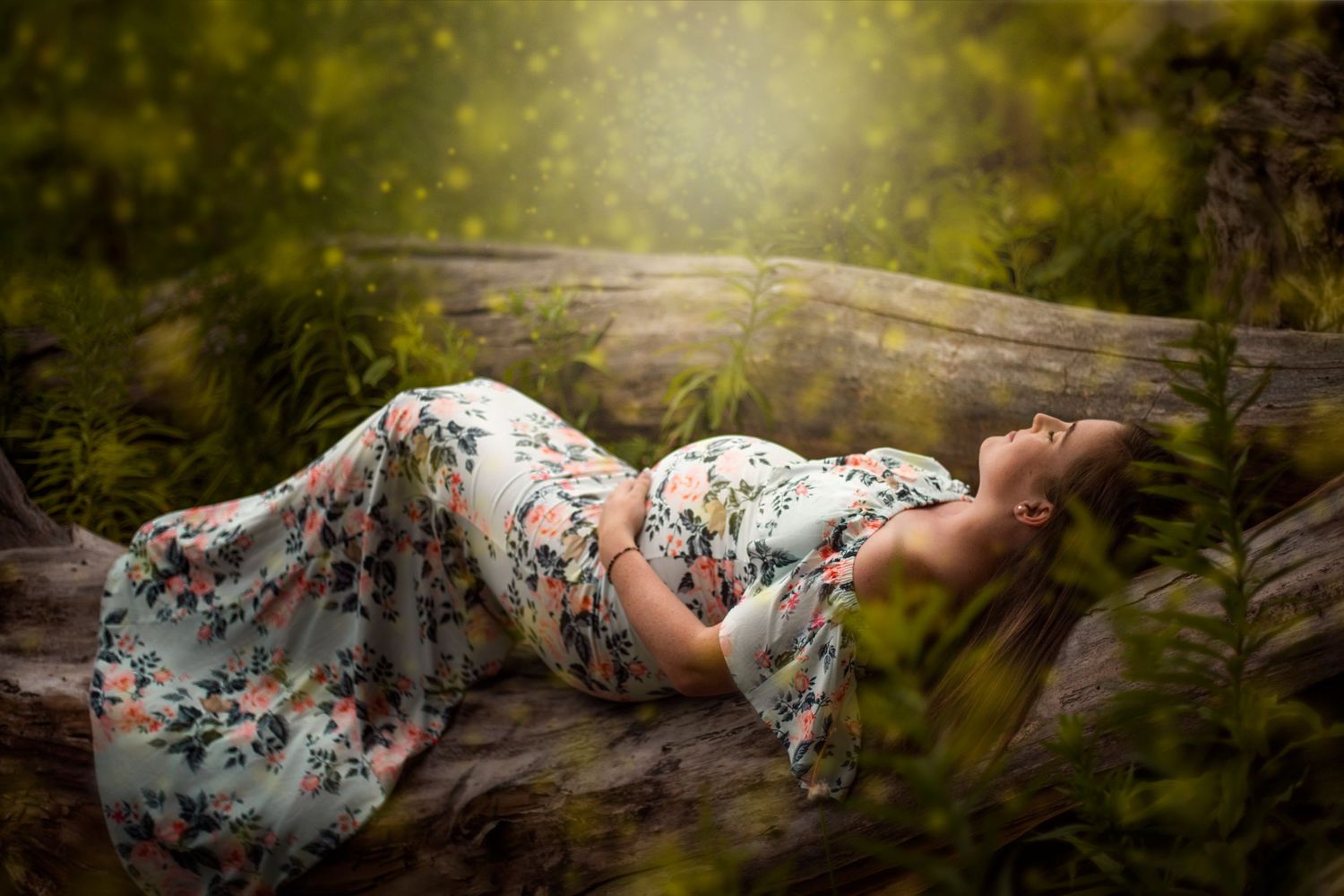 Artistic maternity portrait of a woman in floral dress reclining on rustic wood outdoors.