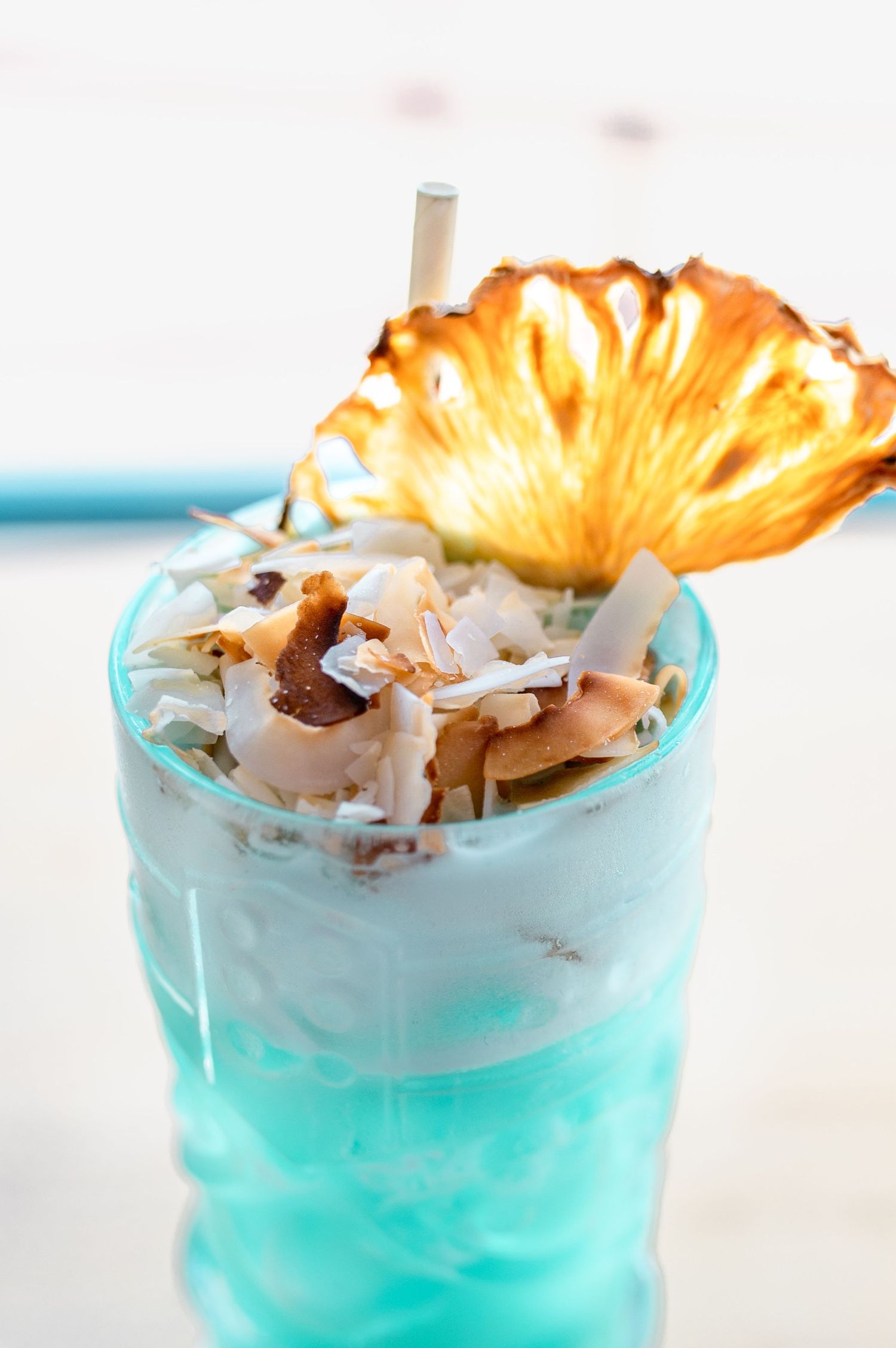 Blue tropical cocktail topped with coconut flakes and garnished with a grilled pineapple slice.