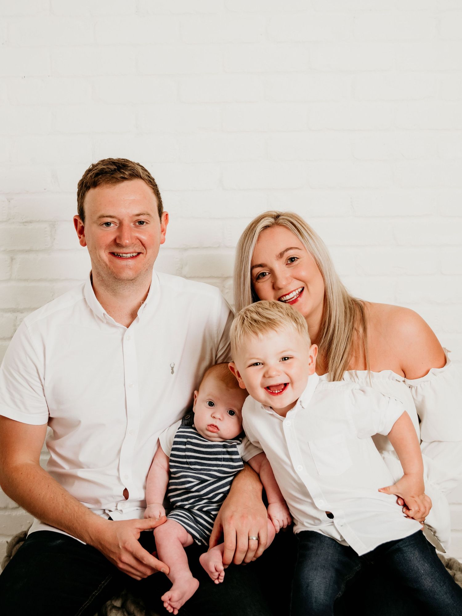 Family portrait session with everyone wearing white against light background.